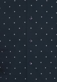 Camicetta blu scuro con un motivo geometrico bianco caratterizzato da piccole forme a diamante. Design classico con bottoni e chiusura abbinata.
