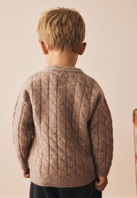 Cable-knit sweater in light brown wool, featuring textured pattern and crew neck. The back shows loose fit and ribbed hem.