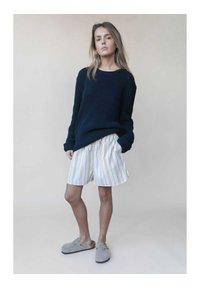 Navy gestrickter Pullover mit gerippter Textur, kombiniert mit weißen Streifen-Shorts und grauen Slippern, die ein lockeres, lässiges Design aufweisen.