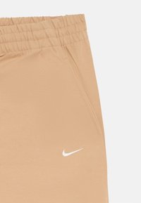 Bež športni hlače iz raztegljive tkanine z elastičnim pasom, stranskima žepoma in belim logotipom Nike na spodnjem levem sprednjem delu.
