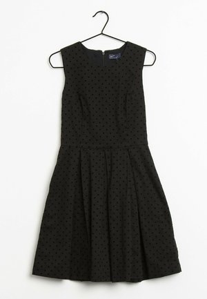 Musta hihaton mekko, jossa istuva yläosa ja levenevä helma. Pinnassa kohollaan olevia mustia pilkkuja. Takana vetoketjukiinnitys.