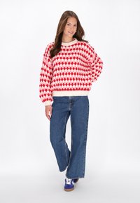 Knit sweater with red and white diamond pattern, round neck, and ribbed cuffs. Paired with high-waisted, wide-leg blue jeans and blue sneakers.