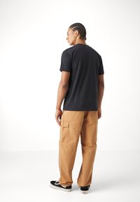 Black cotton t-shirt, relaxed fit, paired with tan cargo pants featuring side pockets. Black sneakers with white soles. Minimalistic background.