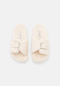 Faux fur slide slippers in a soft cream color, featuring a crisscross design, silver buckle accent, and plush texture.