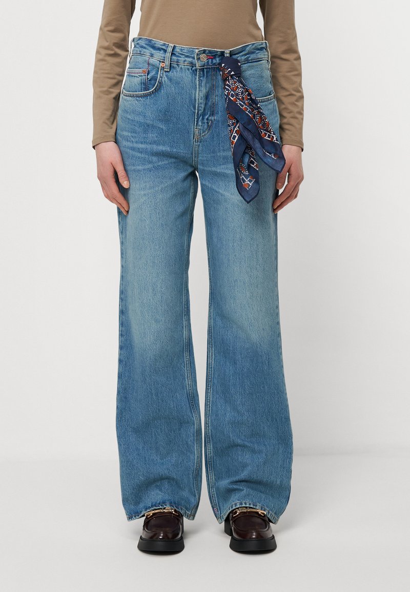 Los jeans de pierna ancha de color azul claro presentan un acabado desgastado, un diseño clásico de cinco bolsillos y una bufanda estampada de color azul oscuro atada a la cintura.