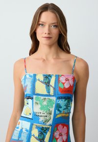 Farbenfrohes blaues Kleid mit dünnen Trägern, das eine Patchwork-Optik mit tropischen Drucken und strukturierten Akzenten zeigt, darunter Papageien und Blumen.