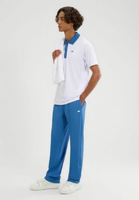 Męski strój sportowy składający się z białej koszulki polo z niebieskim kołnierzykiem i logo, w połączeniu z niebieskimi spodniami sportowymi i białymi trampkami.