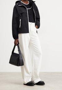 Zwarte lichtgewicht jas met capuchon, witte getailleerde shirt, brede witte broek, zwarte handtas en stevige zwarte schoenen met gestructureerde zolen.