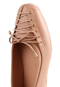Lichtbeige leren ballerina met ronde neus, gouden oogjes, bijpassende veters gestrikt in een strik en gouden veteruiteinden.