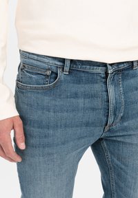 Lichtblauwe denim jeans met een rechte pasvorm. Kenmerken zijn onder andere vijf zakken, oranje stiksels en een lichte verkleuring in de stoftextuur.