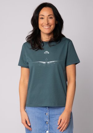 Teal katoenen T-shirt met ronde hals, heeft een witte grafische afbeelding van een figuur en een globe, korte mouwen en een relaxte pasvorm.