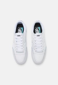 Sneaker bianche Vans con punta perforata, collarino imbottito e lacci piatti. Soletta scura con pois blu e marchio Vans. Design classico a taglio basso.
