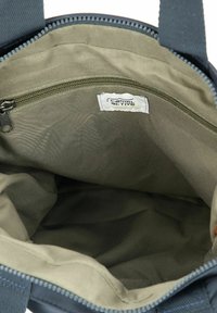 Interior de una bolsa de tela azul oscuro con forro verde oliva. Cuenta con un bolsillo con cremallera y una etiqueta que dice "camel active". Textura suave.