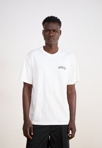 White short-sleeve cotton t-shirt featuring a small black "DICKIES" logo on the chest, relaxed fit, and crew neckline.
