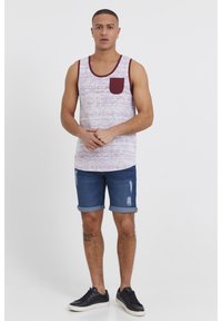 Vit linne med vinröda detaljer och ficka, kombinerad med blå jeansshorts med slitna detaljer, bärs med svarta sneakers.