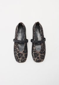 Ballerines noires et beiges à motifs avec un bout arrondi, ornées de perles noires texturées et d'une sangle noire froncée sur le cou-de-pied.