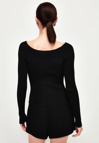 Schwarzes, geripptes Langarmoberteil mit weitem Bootsausschnitt, taillierter Silhouette und strukturiertem Finish, kombiniert mit schwarzen Shorts.