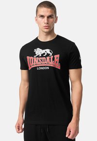 Zwarte katoenen T-shirt met een witte leeuwafbeelding en rode tekst "Lonsdale London". Korte mouwen en een ronde halslijn.