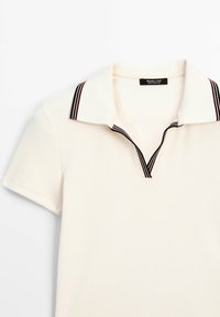 Vit polo t-shirt med ribbad textur, med en svart och vinröd randig krage och en kort V-halsdesign. Varumärkesetikett synlig.