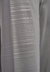 Gros plan sur un tissu sportif gris, présentant une texture lisse avec un dégradé subtil et un motif horizontal, mettant en avant des détails de design moderne.