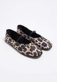 Bailarinas de un patrón de leopardo en beige y negro, con suela plana y una tira decorativa negra a lo largo del empeine.
