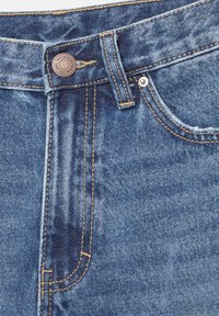 Blue denim jeans with a golden yellow stitching, featuring a metal button closure and angled front pockets.