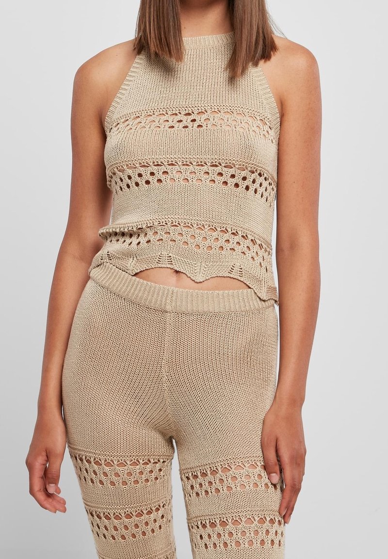 Femme portant un crop top beige en maille sans manches et un short taille haute assorti avec des rayures horizontales en maille ajourée.