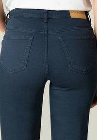 Marineblauwe denim jeans met een middelhoge taille, voorzien van twee achterzakken en een vierkante tan leren label op de tailleband. Gladde textuur.