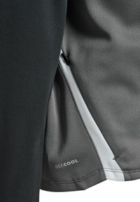 Nahaufnahme von grauem und schwarzem Sportstoff mit Reißverschluss und dem „BEECOOL“-Logo auf dem grauen Bereich nahe dem Saum.