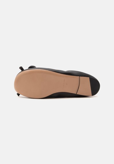 Chaussure plate noire vue de dessous, avec une semelle lisse marron clair et un petit talon carré sur fond blanc.