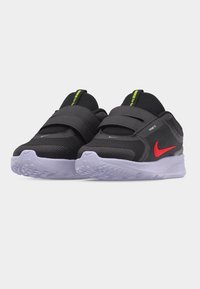 Ζευγάρι μαύρα αθλητικά παπούτσια Nike slip-on με κόκκινο σημάδι Swoosh, λευκή υφή σόλας και λαχανί ταινίες τραβήγματος πάνω σε απλό φόντο.
