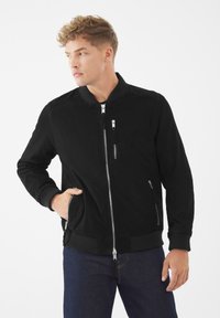 Svart bomberjacka med mjuk textur, som har en hel dragkedja framtill, ribbade manschetter och två sidofickor med dragkedja.