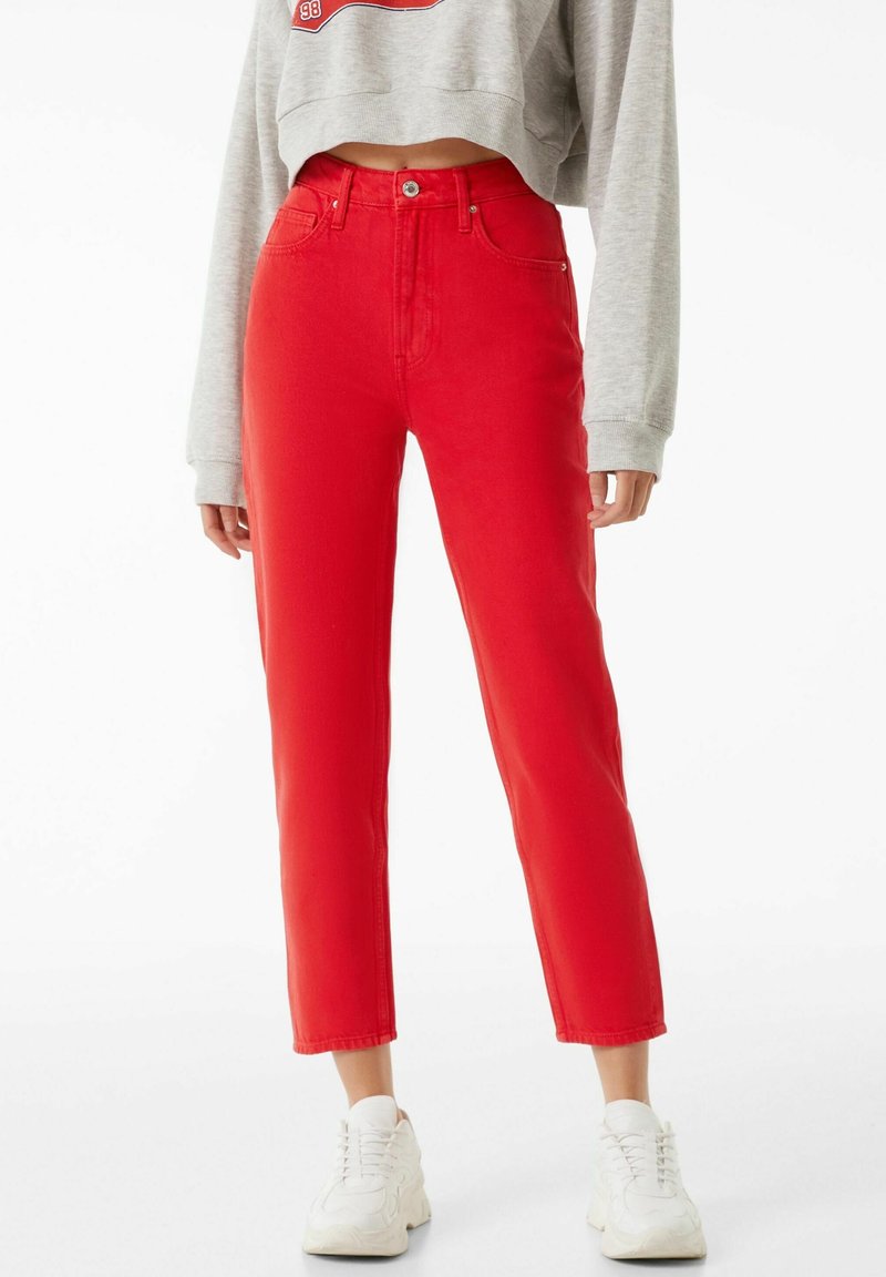 Pantalones vaqueros rojos de cintura alta, con un corte recto, cinco bolsillos y un acabado limpio. Combinados con zapatillas blancas y un suéter corto gris.