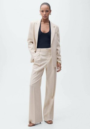 Beige tailored suit with a single-button blazer, wide-legged trousers, and a black fitted top. Smooth fabric texture and minimalistic design.
