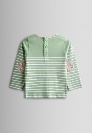 Dlhá košeľa svetlozelenej farby s bielymi pruhmi, s kvetinovým lemom okolo krku a vzorovanými záplatami na lakťoch. Na chrbte vidieť štyri gombíky.