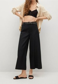 Černé široké kalhoty s texturovaným černým páskem se zaoblenou sponou. Vhodně doplněno béžovou volnou košilí a černými sandály.