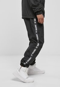 Schwarze Sporthose mit weißem "STARTER"-Logo, das die Seite entlang verläuft, aus leichtem Material und mit lässiger Passform. Kombiniert mit weißen High-Top-Sneakern.