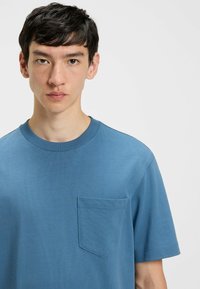 Maglietta a maniche corte con scollo rotondo di un vivace colore blu, dotata di una piccola tasca sul petto e di un tessuto testurizzato con striature sottili.