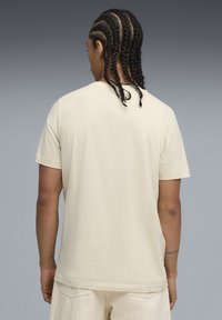 Beige bomulds-T-shirt med korte ærmer og lige snit, der har en subtil tekstur og rund udskæring, set fra ryggen.