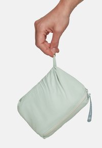Pochette in pelle morbida verde chiaro con chiusura a cerniera e un piccolo anello in tessuto per appendere. Texture liscia, forma rettangolare e design minimale.