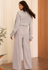 Svetlo šedé široké nohavice s elastickým pásom v kombinácii s mäkkým šedým svetríkom. Hladká textúra, voľný strih, minimálne detaily.