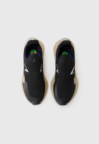 Black athletic shoes with a textured upper, light beige sole, and green-blue accents. Features a perforated design and minimalistic branding.