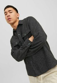 Camicia nera con bottoni, caratterizzata da un sottile motivo a pois bianchi, tasche sul petto e maniche lunghe, realizzata in tessuto testurizzato. Vestibilità casual.