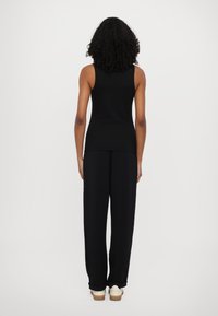 Top nero senza maniche e pantaloni neri larghi. Tessuto liscio, design semplice, indossati con scarpe chiare e suola naturale.