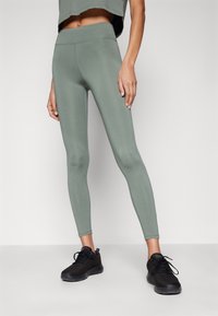 Leggings verde chiaro con vita alta, realizzati in materiale elasticizzato. Abbinati a scarpe sportive nere con design in rete.