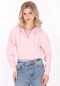 Gekürzter rosa Hoodie mit einem Reißverschluss vorne, ausgestattet mit einer hellblauen Kordelzugkapuze, aus weichem Stoff, kombiniert mit hochgeschnittenen blauen Jeans.