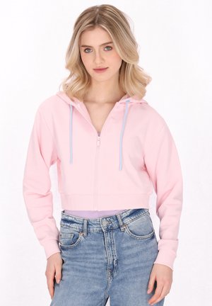 Gekürzter rosa Hoodie mit einem Reißverschluss vorne, ausgestattet mit einer hellblauen Kordelzugkapuze, aus weichem Stoff, kombiniert mit hochgeschnittenen blauen Jeans.