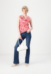 Blomstrete rosa ermeløs topp med cowl-halsutskjæring; blå svingjeans; hvit håndveske; kremfargede kitten heels; lys bakgrunn.
