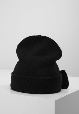 Bonnet en tricot noir avec un bord plié et un détail de nœud sur le côté, présenté sur une surface blanche.