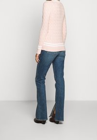 Vaaleanpunainen palmikkoneule, jossa valkoiset raidat helmassa ja hihansuissa, yhdistetty sinisiin levenevään lahkeeseen oleviin farkkuihin ja ruskeisiin korollisiin kenkiin.